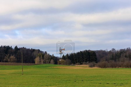 Téléchargez les photos : Old windmill on a tower on the meadows near the Archabbey of St. Ottilien in Bavaria in front of a forest under cloudy sky - en image libre de droit