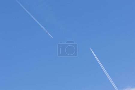Foto de Two planes with white contrail meet head-on in blue sky - Imagen libre de derechos