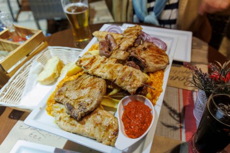 Photo for Croatian grill plate with chips rice ayvar and grilled meat in a restaurant in Rovinj in the evening - Royalty Free Image