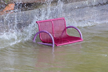 Téléchargez les photos : Un banc de parc est inondé par les hautes eaux et se tient dans l'eau tandis que les vagues éclaboussent dessus - en image libre de droit