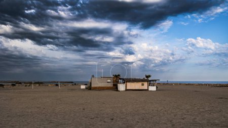 Photo for Dark storm clouds gather above a beach bar on the deserted sandy beach of Saint Marie de la Mer - Royalty Free Image