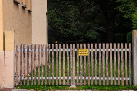 Téléchargez les photos : Un rouge-gorge est assis sur une porte de jardin en lattes de bois avec un panneau avec le texte allemand : Gardez la sortie libre - en image libre de droit