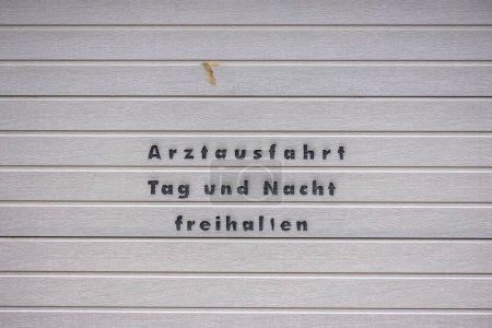 Téléchargez les photos : Porte de garage grise avec lettrage noir : le texte allemand garde la sortie du médecin claire jour et nuit - en image libre de droit