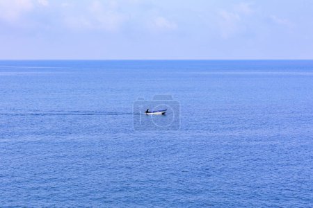 Téléchargez les photos : Un bateau de pêche solitaire navigue sur la mer bleue par une journée ensoleillée avec un ciel bleu en face de la ville croate Rovinj - en image libre de droit
