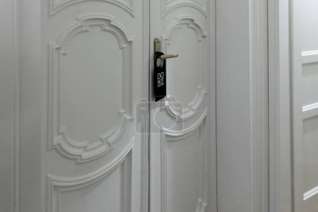 Photo for White door of a hotel room with a black sign on the door handle with the English text do not disturb - Royalty Free Image