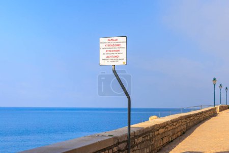 Foto de Pared de piedra en el paseo marítimo de la ciudad croata de Rovinj en un día soleado con cielo azul con un cartel en el que está escrito en varios idiomas el texto: Atención, escalada en la pared está prohibido - Imagen libre de derechos