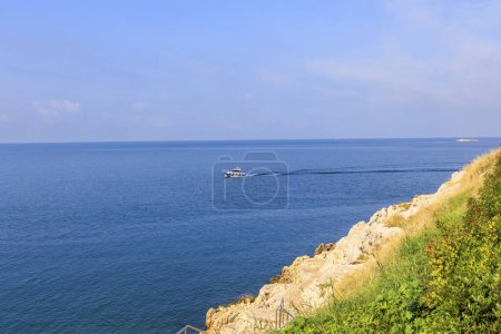 Téléchargez les photos : Un bateau de pêche solitaire navigue sur la mer bleue par une journée ensoleillée avec un ciel bleu en face de la ville croate Rovinj - en image libre de droit
