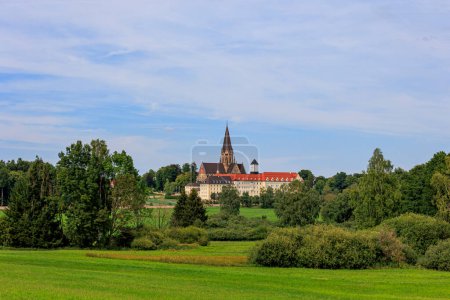 Foto de The church tower of St. Ottilien Monastery in Bavaria between forests and meadows under white blue sky - Imagen libre de derechos