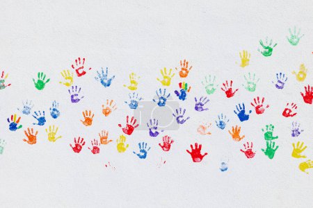 Téléchargez les photos : Modèle d'empreintes de mains colorées a été estampillé sur un mur blanc avec des mains d'enfants de couleur - en image libre de droit