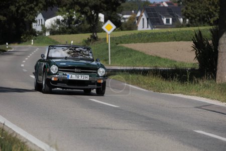 Foto de Green Triumph TR6 de los años 70 conduciendo en una carretera de campo cerca del castillo de Blumenthal durante el rallye de autos clásicos Fuggerstadt Classics, Alemania, Augsburgo, 24 de septiembre de 2023 - Imagen libre de derechos
