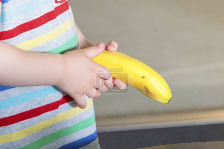 Photo for Caucasian  Child hand holds a yellow unpeeled banana caucasian - Royalty Free Image