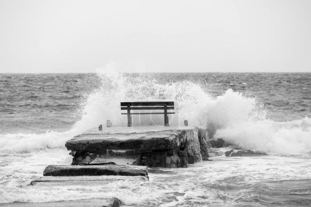 Photo for A resting bench in the middle of the waves on the island of Corfu near the town of Arillas under blue skies and heavy seas - Royalty Free Image