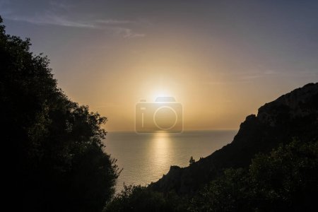 Téléchargez les photos : Le soleil se couche doré sur la mer contre la silhouette de la côte aux ruines d'Angelokastro près d'Agios Spiridon sur l'île de Corfou - en image libre de droit