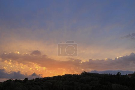 Foto de Colorido atardecer en la bahía de Agios Georgios con nubes oscuras frente a un cielo intensamente anaranjado con nubes oscuras de forma extraña en la isla de Corfú - Imagen libre de derechos