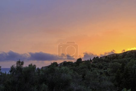 Téléchargez les photos : Coucher de soleil coloré dans la baie d'Agios Georgios avec des nuages sombres en face d'un ciel intensément orange avec des nuages tordus sombres de forme étrange sur l'île de Corfou - en image libre de droit