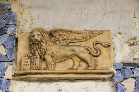 Téléchargez les photos : Un relief de pierre d'un lion ailé avec un livre à la main sur un mur sur l'île de Corfou - en image libre de droit