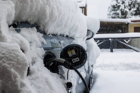 Une voiture électrique recouverte de neige profonde est chargée d'une fiche de recharge de type 2 en hiver, Allemagne, Augsbourg, 2 décembre 2023
