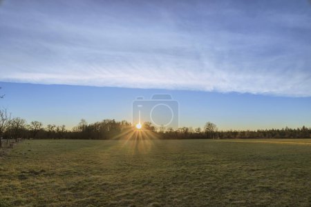 Foto de Los rayos del sol naciente de la mañana brillan a través de los árboles en los campos y prados de Siebenbrunn, el distrito más pequeño de la ciudad de Fugger de Augsburgo - Imagen libre de derechos
