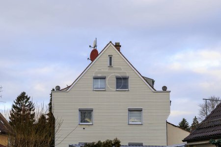Téléchargez les photos : Une maison blanche avec une antenne parabolique rouge et des lambris extérieurs sur un terrain avec des arbres et une route à Haunstetten, un quartier de la ville Fugger d'Augsbourg - en image libre de droit