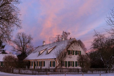 Téléchargez les photos : Petite ferme avec lumières de Noël à la lisière de la forêt à Siebenbrunn, le plus petit quartier de la ville Fugger d'Augsbourg, par une journée d'hiver avec des nuages rouge vif au lever du soleil - en image libre de droit