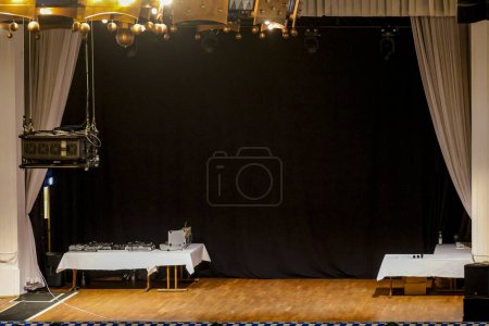 Photo for An empty stage with projector tables with white tablecloths wooden parquet and a black curtain in the background - Royalty Free Image