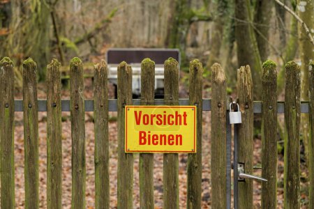 An old mossy wooden fence in the forest near Siebenbrunn is locked with a padlock and bears a sign with the German text Beware of bees