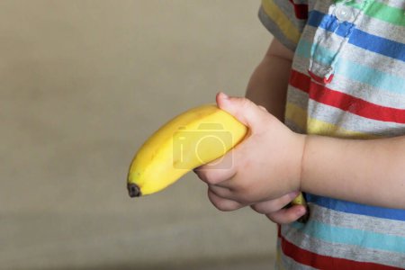 Photo for Caucasian  Child hand holds a yellow unpeeled banana caucasian - Royalty Free Image