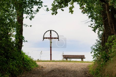 Photo for A field cross with depiction of the crucified Christ next to a rest bench on a field path near Friedberg near Augsburg, Germany - Royalty Free Image