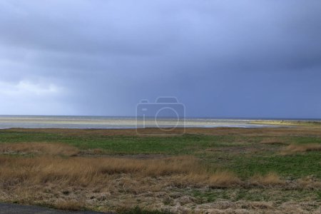 View over the dunes and the beach to the sea in the Dutch town of Den Helder on a stormy day with rain and clouds,