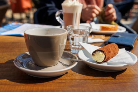 Tasse Kaffee und Schokorolle mit Sahnefüllung in einem Straßencafé in der niederländischen Stadt Delft im Frühling