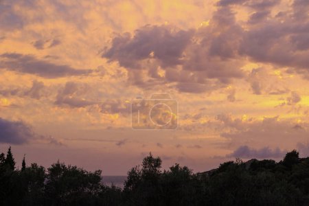Téléchargez les photos : Coucher de soleil coloré dans la baie d'Agios Georgios avec des nuages sombres en face d'un ciel intensément orange avec des nuages tordus sombres de forme étrange sur l'île de Corfou - en image libre de droit
