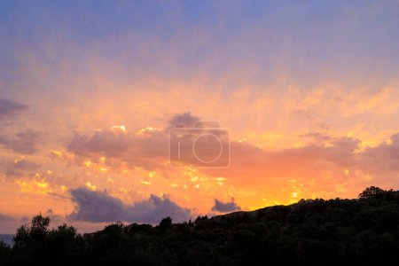 Coucher de soleil coloré dans la baie d'Agios Georgios avec des nuages sombres en face d'un ciel intensément orange avec des nuages tordus sombres de forme étrange sur l'île de Corfou