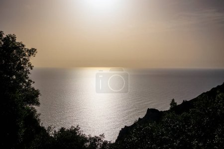 Téléchargez les photos : Le soleil se couche doré sur la mer contre la silhouette de la côte aux ruines d'Angelokastro près d'Agios Spiridon sur l'île de Corfou - en image libre de droit