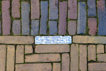 Brick pavement on the market square in the city of Delft in the Netherlands with an inscribed stone in which the word earth is written in Delft blue in many languages