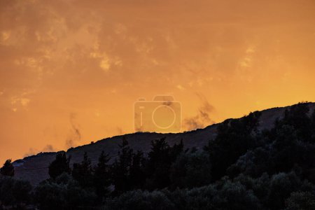 Coucher de soleil coloré dans la baie d'Agios Georgios avec des nuages sombres en face d'un ciel intensément orange avec des nuages tordus sombres de forme étrange sur l'île de Corfou