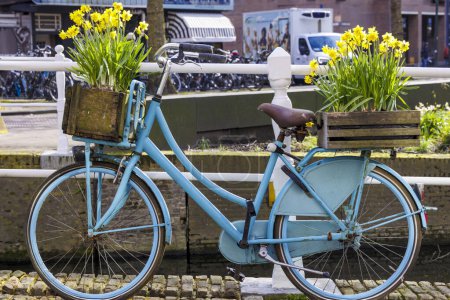 Ein niederländisches blaues Damenfahrrad mit gelben Narzissen steht an einem Geländer in der niederländischen Stadt Delft