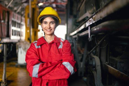 Téléchargez les photos : Ingénierie femmes dans la machine de fonctionnement uniforme de sécurité à l'usine industrielle et debout avec sourire sur le lieu de travail - en image libre de droit