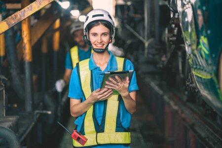 Téléchargez les photos : Belle ingénieure en usine portant un casque blanc et des vêtements de travail et une tablette à main sur le lieu de travail - en image libre de droit
