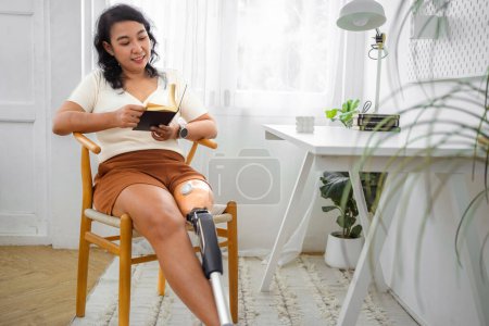 Téléchargez les photos : Femme avec prothèse jambe livre de lecture dans la chambre à la maison - en image libre de droit