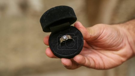 Mann hält schönen Diamantring mit schwarzem Ring-Gehäuse HD