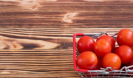 Los tomates pequeños de guinda en la cesta de la compra. Sobre un fondo de madera quemada. El concepto de comprar verduras de un agricultor en línea. Foto de alta calidad