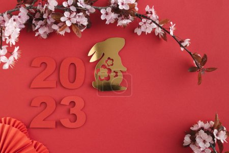 Téléchargez les photos : Nouvel An chinois, année du lapin. Année 2023 avec lapin doré et papier découpés éventails avec des fleurs de prunes naturelles. Espace de copie. Vue du dessus. - en image libre de droit
