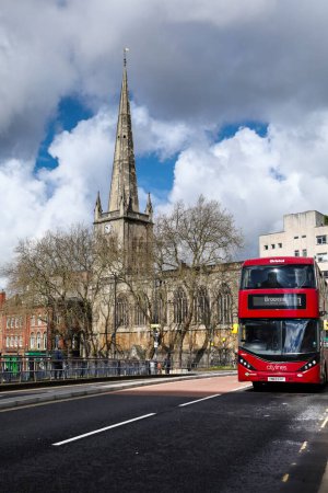Foto de Bristol, Inglaterra 30 de marzo de 2024: Autobús rojo típico que cruza el puente de Bristol. Iglesia de San Nicolás en el fondo - Imagen libre de derechos