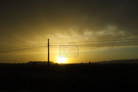 Sun hiding on the horizon at sunset between reed beds and power lines in Spain