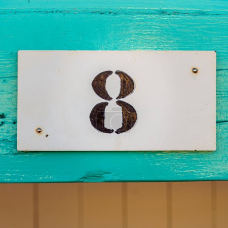 Téléchargez les photos : Number eight on a white plate, attached to a wooden plank, house number sign. - en image libre de droit