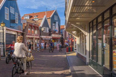 Photo for Volendam, Netherlands - July 13, 2022: Street scene in Volendam on the Haven in the center of the North Holland tourist village. Tourists walk through the shopping street between the cycling residents - Royalty Free Image