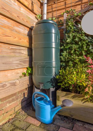 A green rain barrel with a blue watering can in a garden