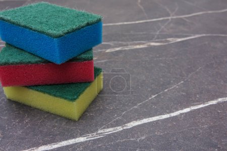 Téléchargez les photos : Trois éponges de nettoyage colorées sur un fond de marbre foncé - en image libre de droit