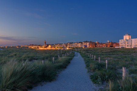Foto de Katwijk aan Zee, Países Bajos - 11 de junio de 2022: Puesta de sol con la hora azul en Katwijk aan Zee con sendero desde las dunas hasta el bulevar. - Imagen libre de derechos