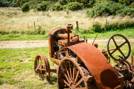 Foto de Tractor agrícola vintage desertó y se oxidó en el claro en el campo de arbustos y colinas de South Island. - Imagen libre de derechos